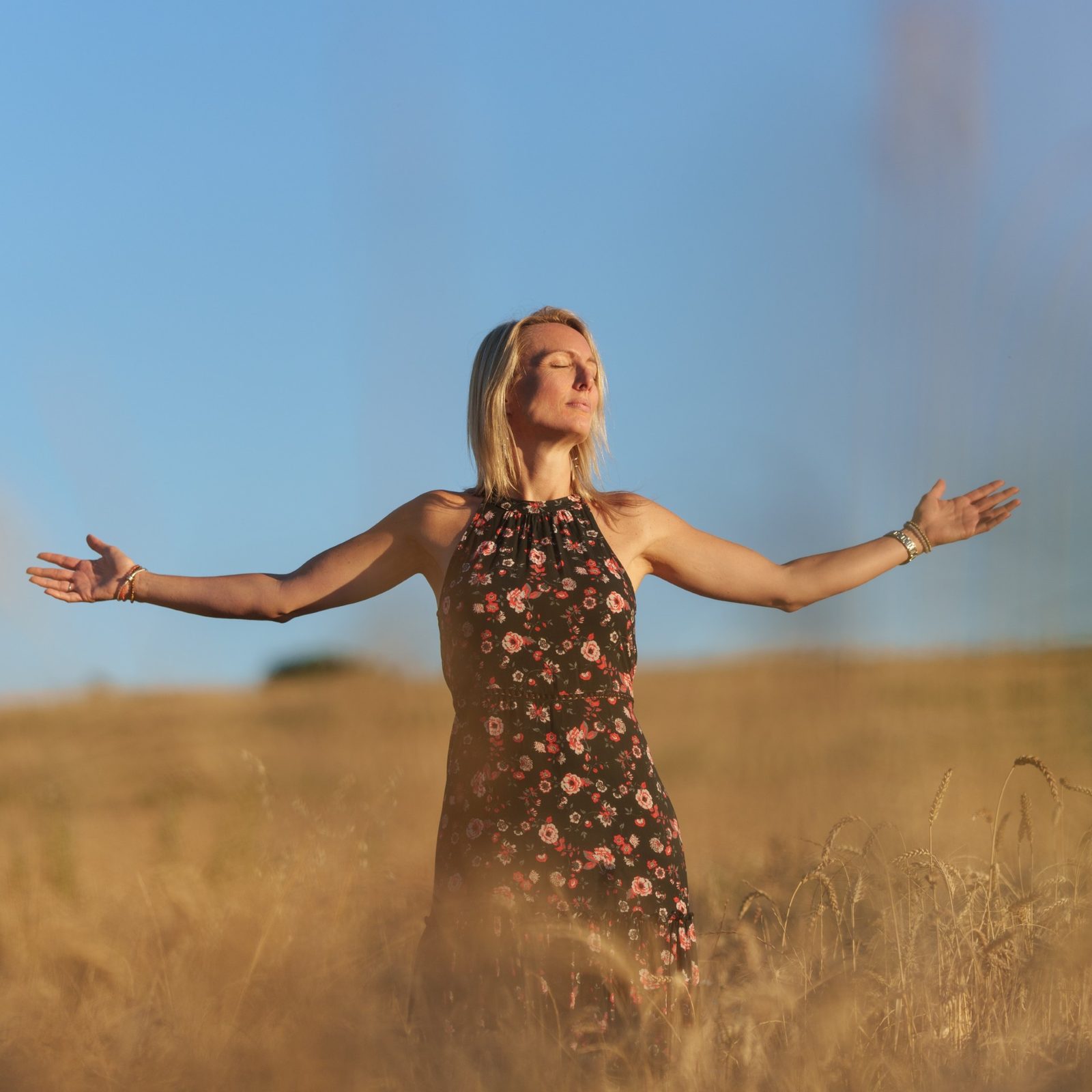 Femme apaisée, bras ouverts dans un champ au soleil — se libérer du stress et de la charge mentale par l'hypnose